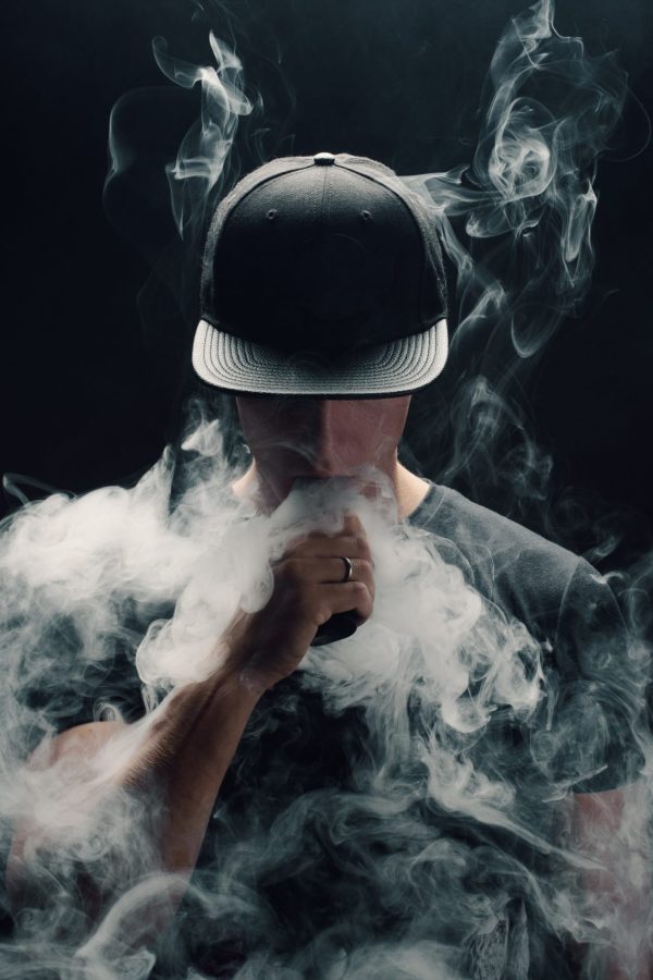 Vape man. Portrait of a handsome young white guy in a modern black cap vaping and letting off puffs of steam from an electronic cigarette